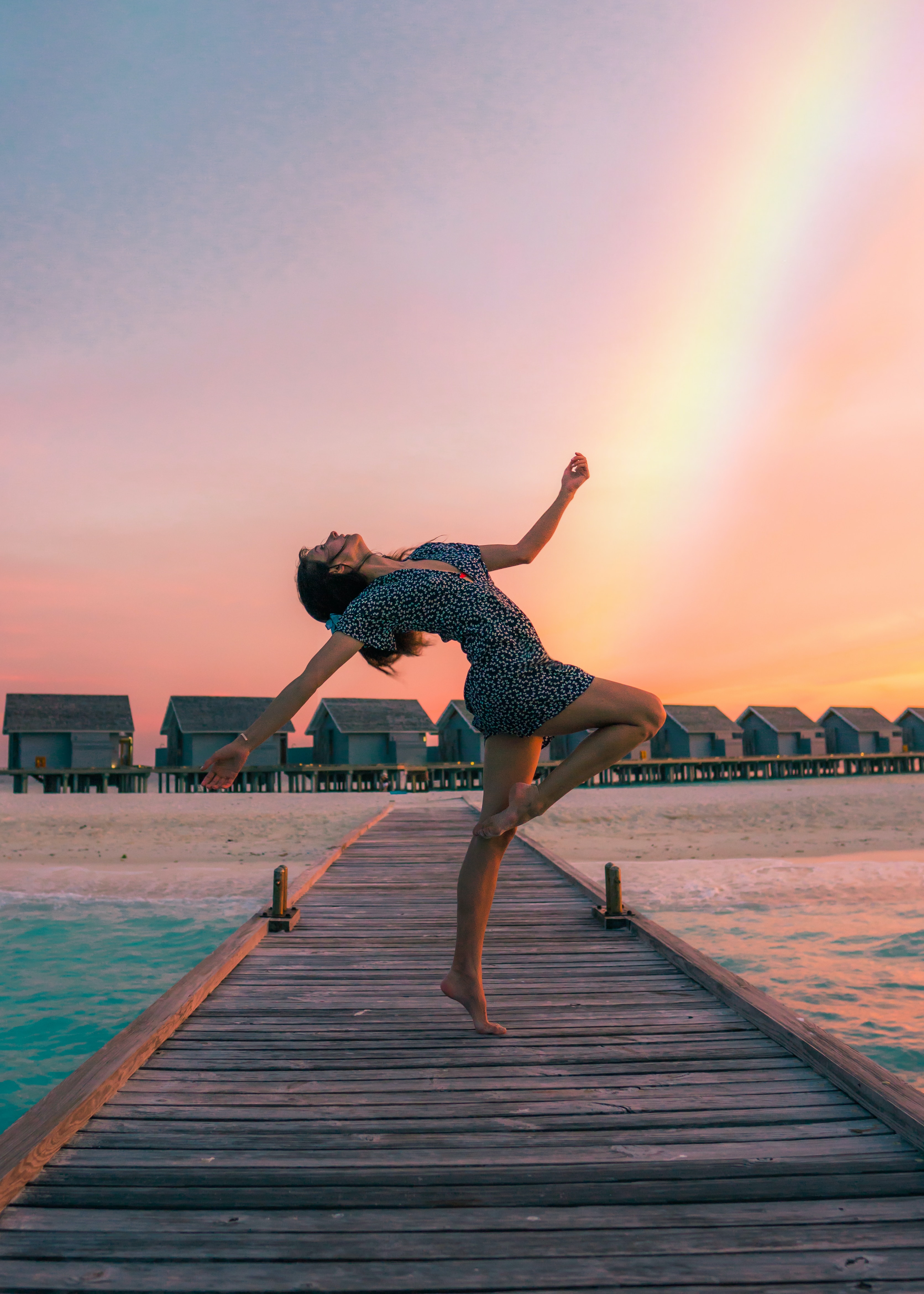 A woman dances on a dock in front of a rainbow. Photographer: Drew Collins.
